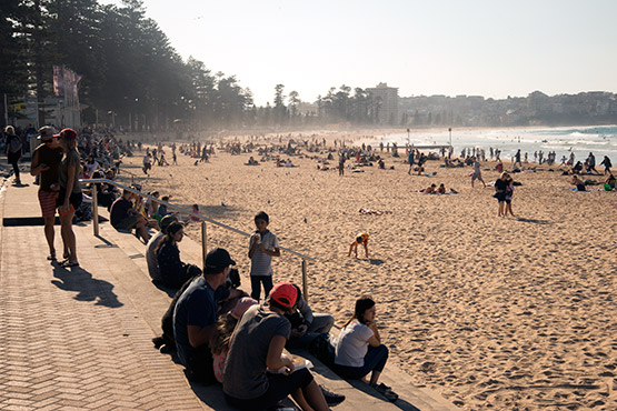 People sit and watch happenings at Manly Beach, Sydney